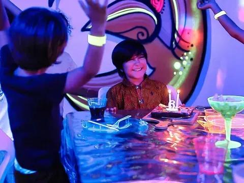 Enfant souriant devant son gâteau d'anniversaire aux bougies, dans une salle éclairée en lumière noire