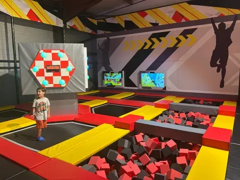 Jeune enfant sur un trampoline près d'une fosse à cubes de mousse, avec une cible interactive murale