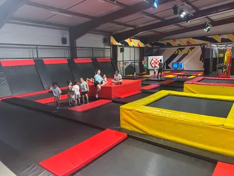 Vaste salle de trampolines bordée de mousses jaunes et rouges, où des enfants et des adolescents sautent sous une charpente métallique